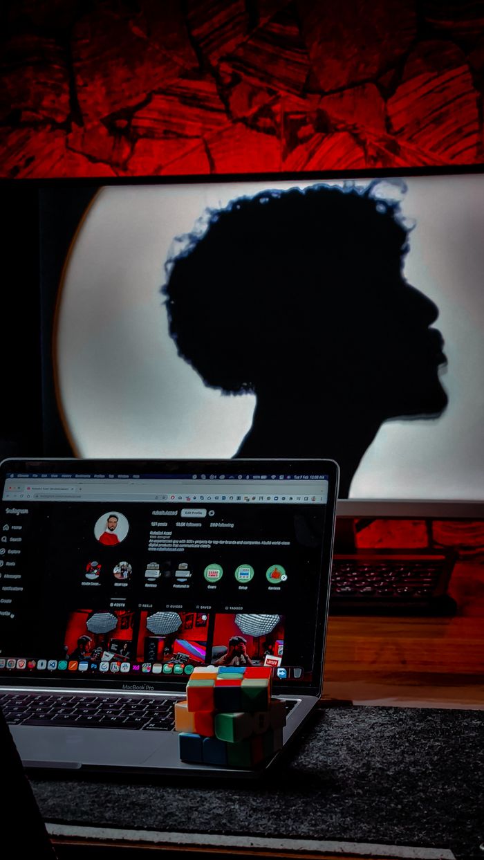Silhouette of person behind laptop with Rubik's cube on desk, modern studio setup.